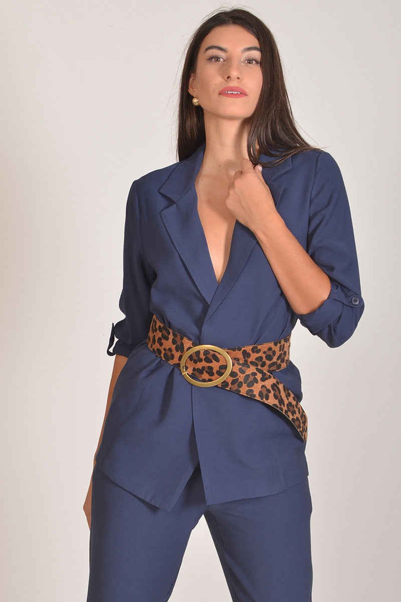 Γυναίκα που φοράει μπλε σακάκι από ύφασμα Tencel, συνδυασμένο με παντελόνι στο ίδιο ύφασμα και χρώμα, και λεοπάρ φαρδιά ζώνη πάνω από το σακάκι.