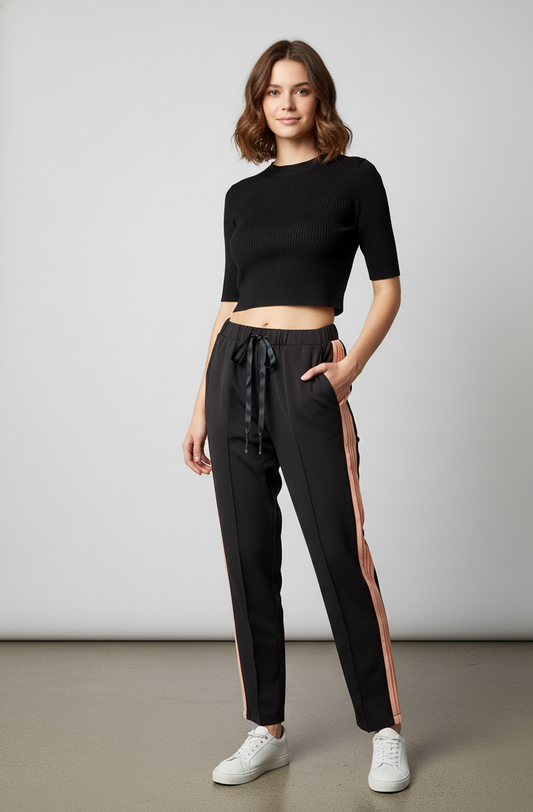 Μαύρο γυναικείο παντελόνι από ύφασμα μουσελίνας διπλό. Δεν διαφανίζει. Στις πλαϊνές ραφές, έχει ρίγα από ροζ μουσελίνα. Στη μέση έχει λάστιχο και κορδόνι. Το παντελόνι έχει τσέπες. Το μοντέλο το έχει συνδυάσει με κροπ τοπ μαύρο και λευκά sneakers